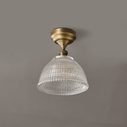 A Clérachic ceiling light seen straight on against a grey ceiling, the clear glass dome hanging below a round brass canopy.