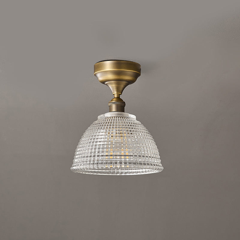 This Clérachic ceiling light at a slight angle, showing the clear grid-cut dome and the antique brass stem against a grey ceiling.