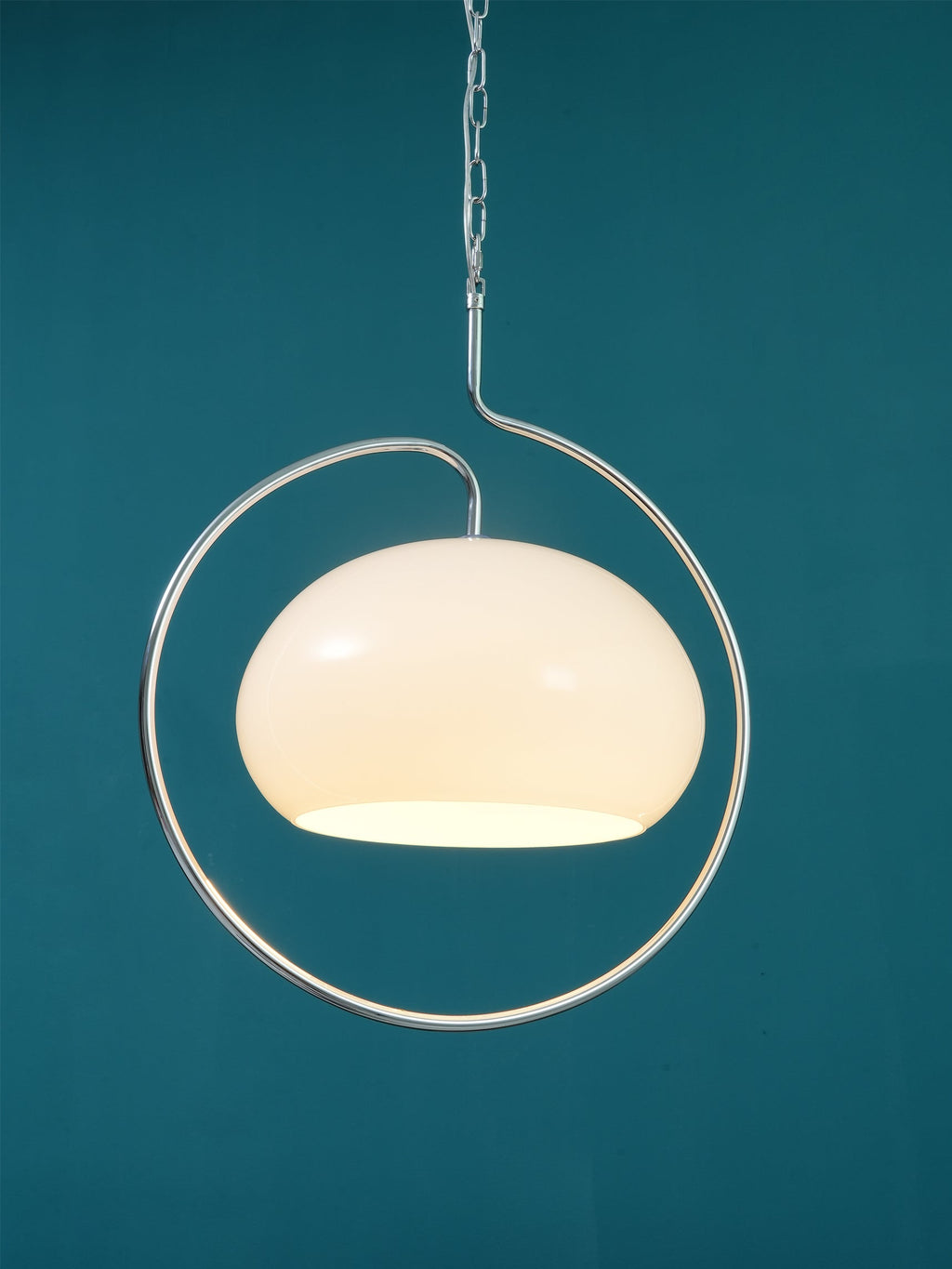 Close view of a white glass Clérachic pendant with a chrome loop, glowing softly against a deep teal wall.