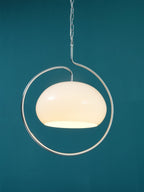 Close view of a white glass Clérachic pendant with a chrome loop, glowing softly against a deep teal wall.