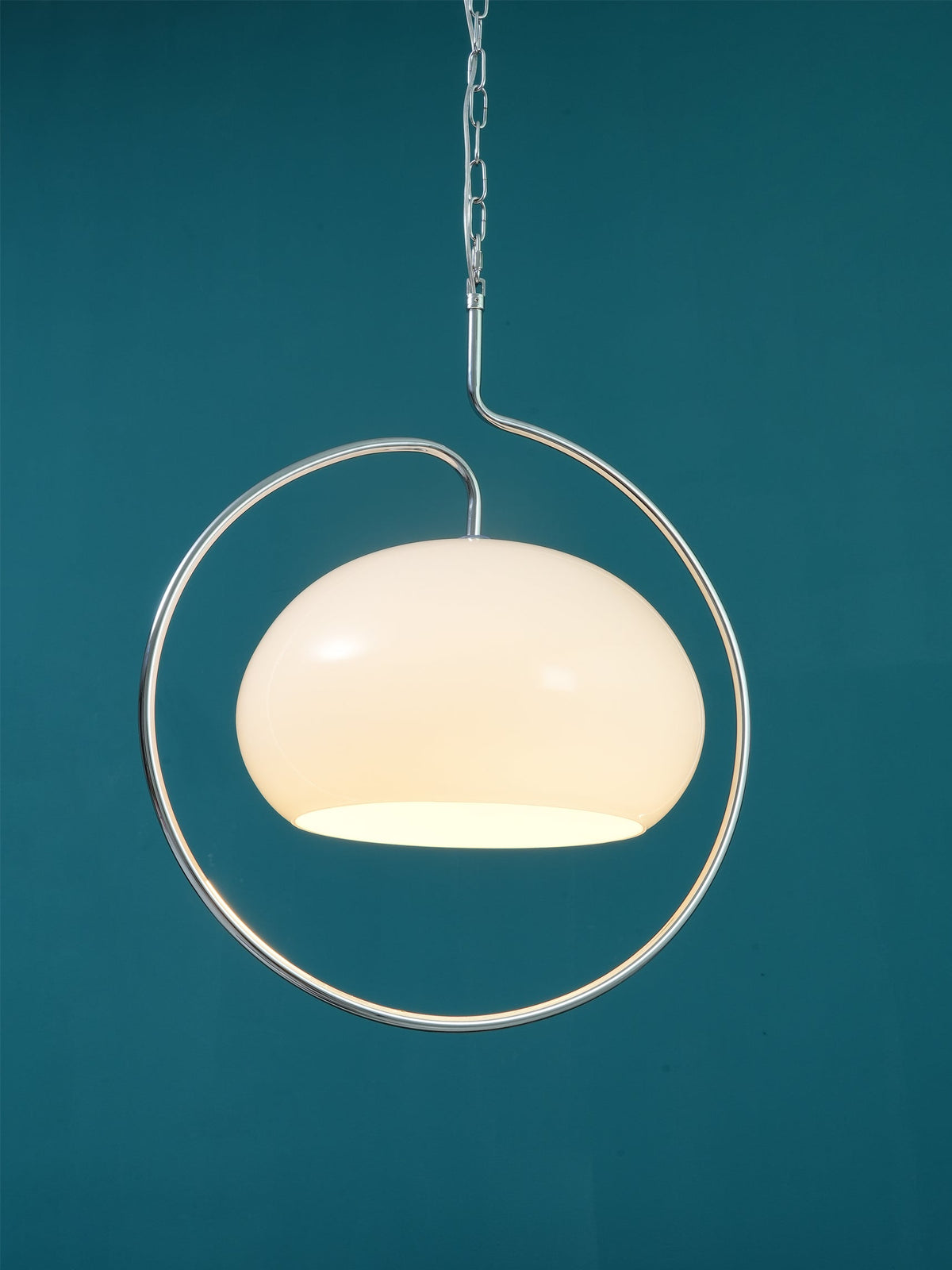 Close view of a white glass Clérachic pendant with a chrome loop, glowing softly against a deep teal wall.