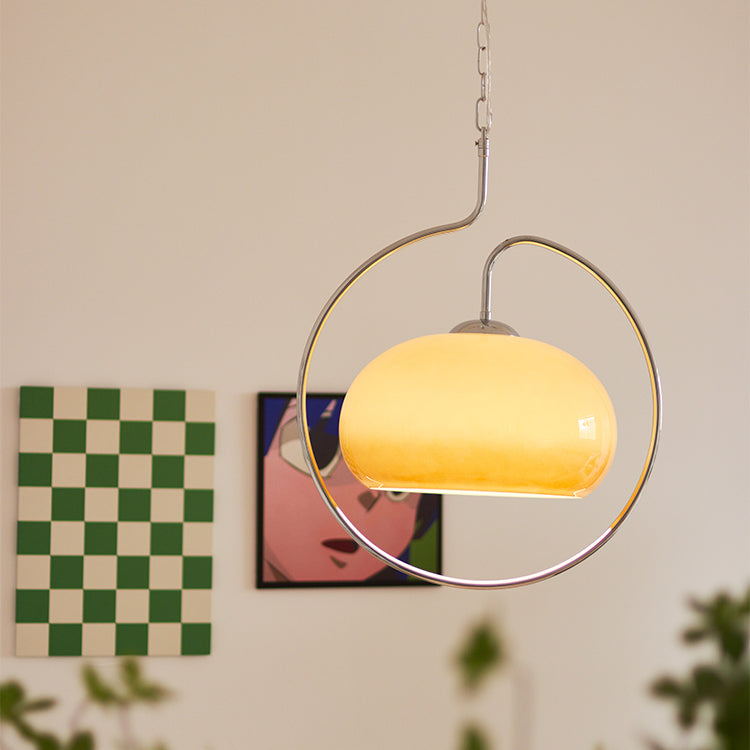 Brown glass Clérachic pendant lit warm cream, with its chrome ring slightly blurred and a green chequered print behind.