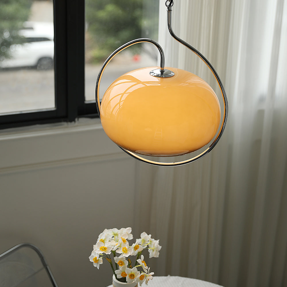 Brown glass Clérachic pendant in a looping chrome frame, seen in daylight beside a window with a vase of white narcissi below.