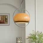 Brown glass Clérachic pendant in a chrome loop, hanging by a pale wall with a framed picture and a mirrored-bead lamp below.