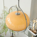 Close view of the brown glass dome on this Clérachic pendant, with its chrome collar and curved arm, and a bead-shaped lamp behind.