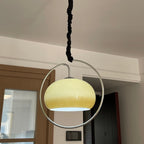 Clérachic glass pendant lit yellow-cream inside a chrome ring, hung from a black fabric-wrapped cord in a hallway with a timber door.