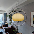 Clérachic pendant with a pale yellow glass dome inside a chrome ring, hung in a living room beside a tall bamboo plant and a framed print.