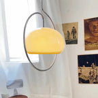 Clérachic glass pendant lit yellow-cream in its chrome ring, beside a sheer curtain and poster-style prints on the wall.