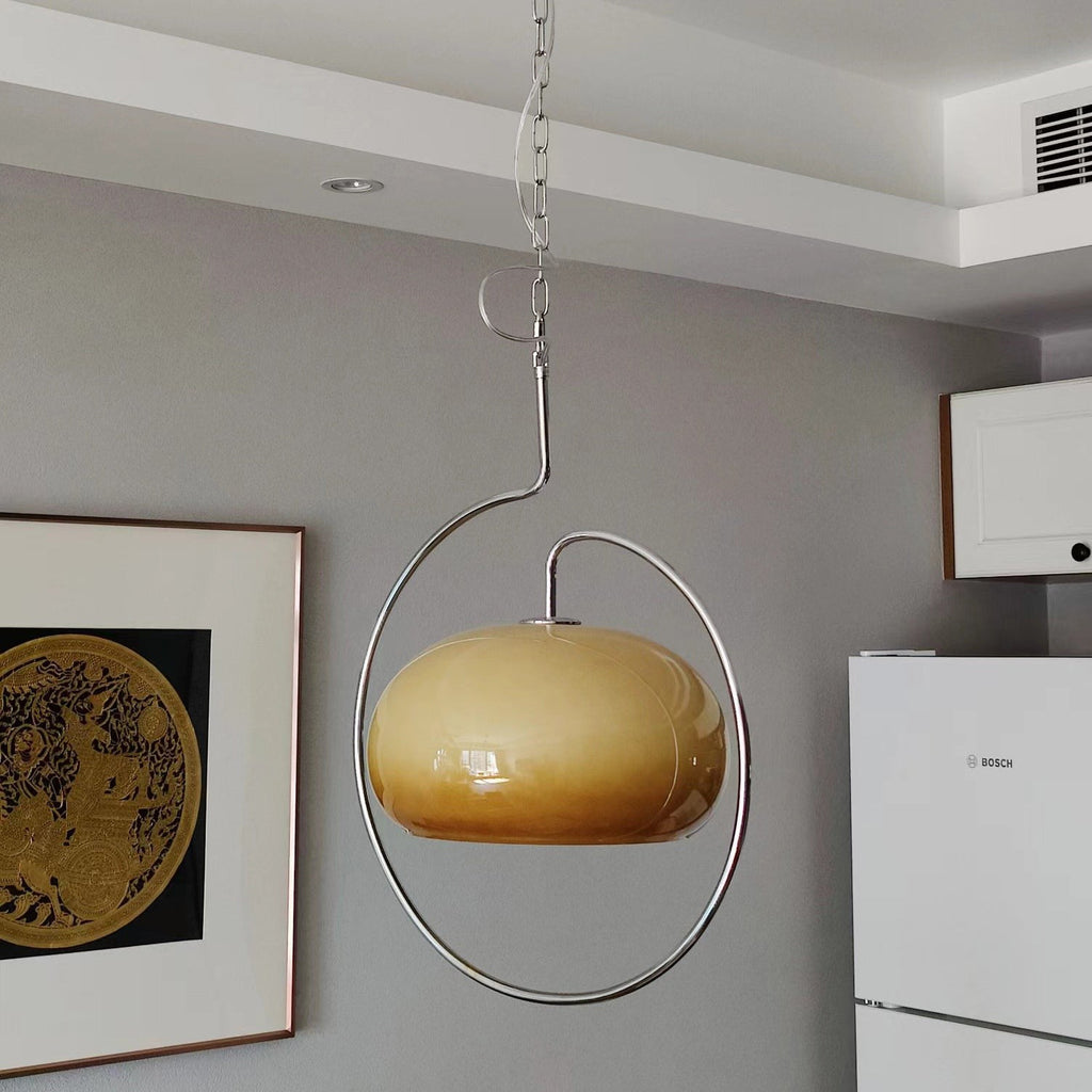 Brown glass Clérachic pendant with a gradient from caramel to cream, in a chrome ring against a grey wall with a framed print.