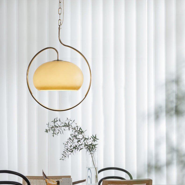 Clérachic pendant with a pale yellow glass dome and a champagne-toned ring, in front of floor-length white curtains and a dining table.