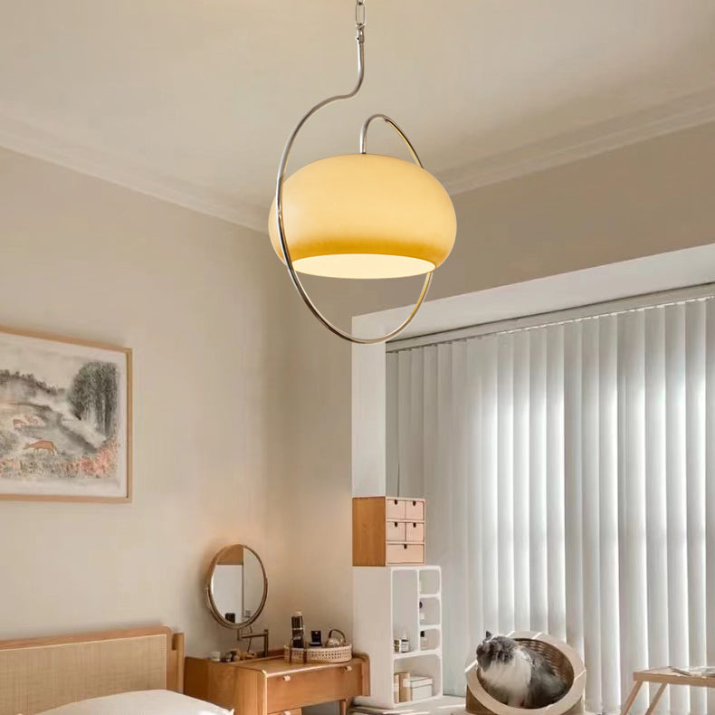 Clérachic glass pendant lit warm white above a bedroom corner, with vertical blinds, a rattan bed and a small framed landscape.