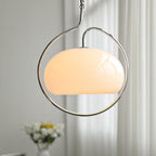 Close view of a white glass Clérachic pendant, glowing softly inside its chrome ring, with a vase of white flowers and curtains behind.