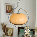 Brown glass Clérachic pendant with a chrome ring in a room with framed pictures, dried pampas stems and a mirrored-bead lamp.