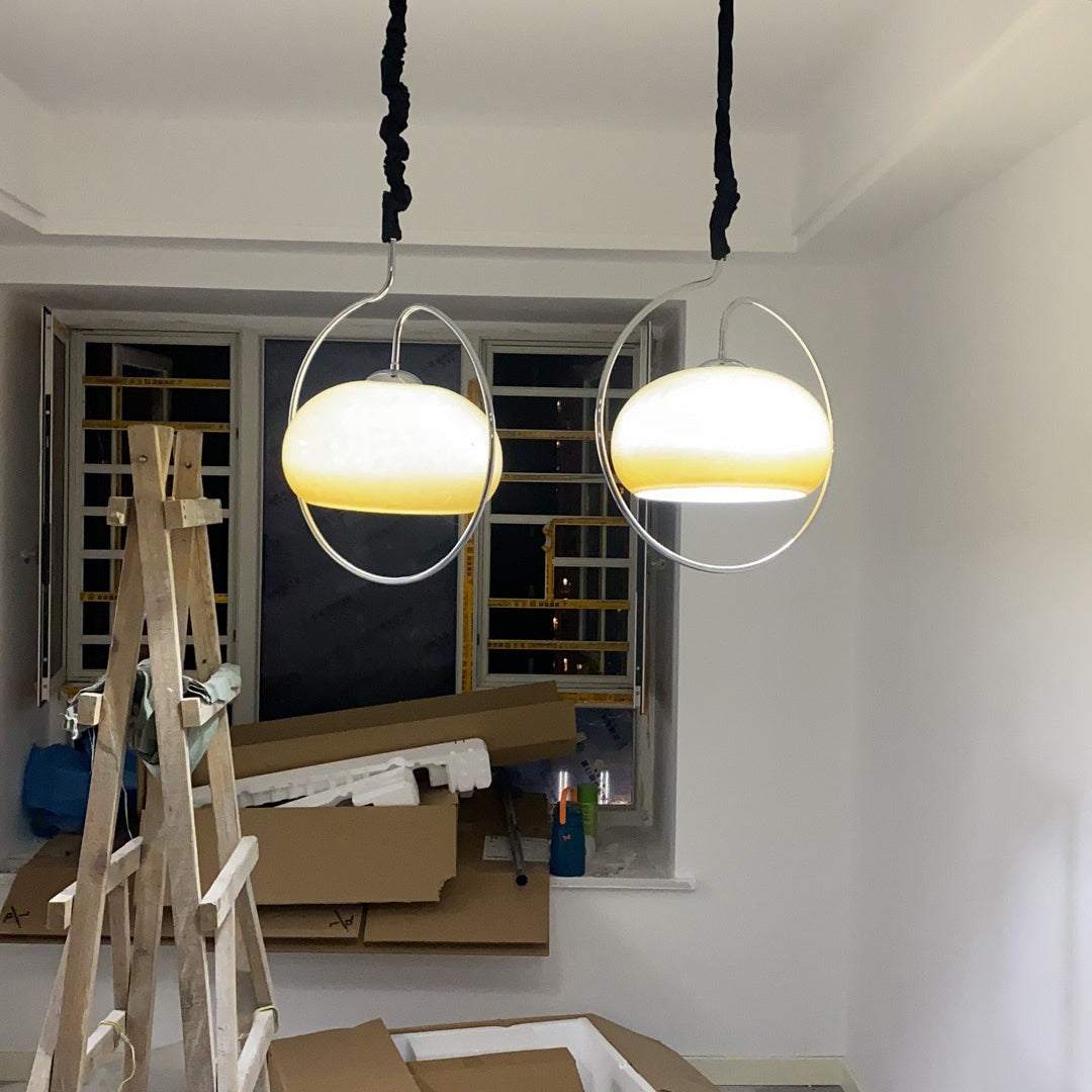 Two Clérachic pendants lit warm white in chrome rings, hung from black cords in a room still being finished, with a ladder and boxes below.