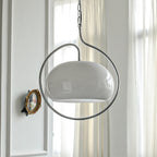 White glass Clérachic pendant inside a chrome ring, hung in a white panelled room next to a small ornate mirror and curtains.