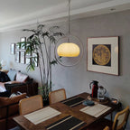 Clérachic pendant with a pale yellow glass dome in a chrome ring, above a wooden dining table in a living room with a tall plant.
