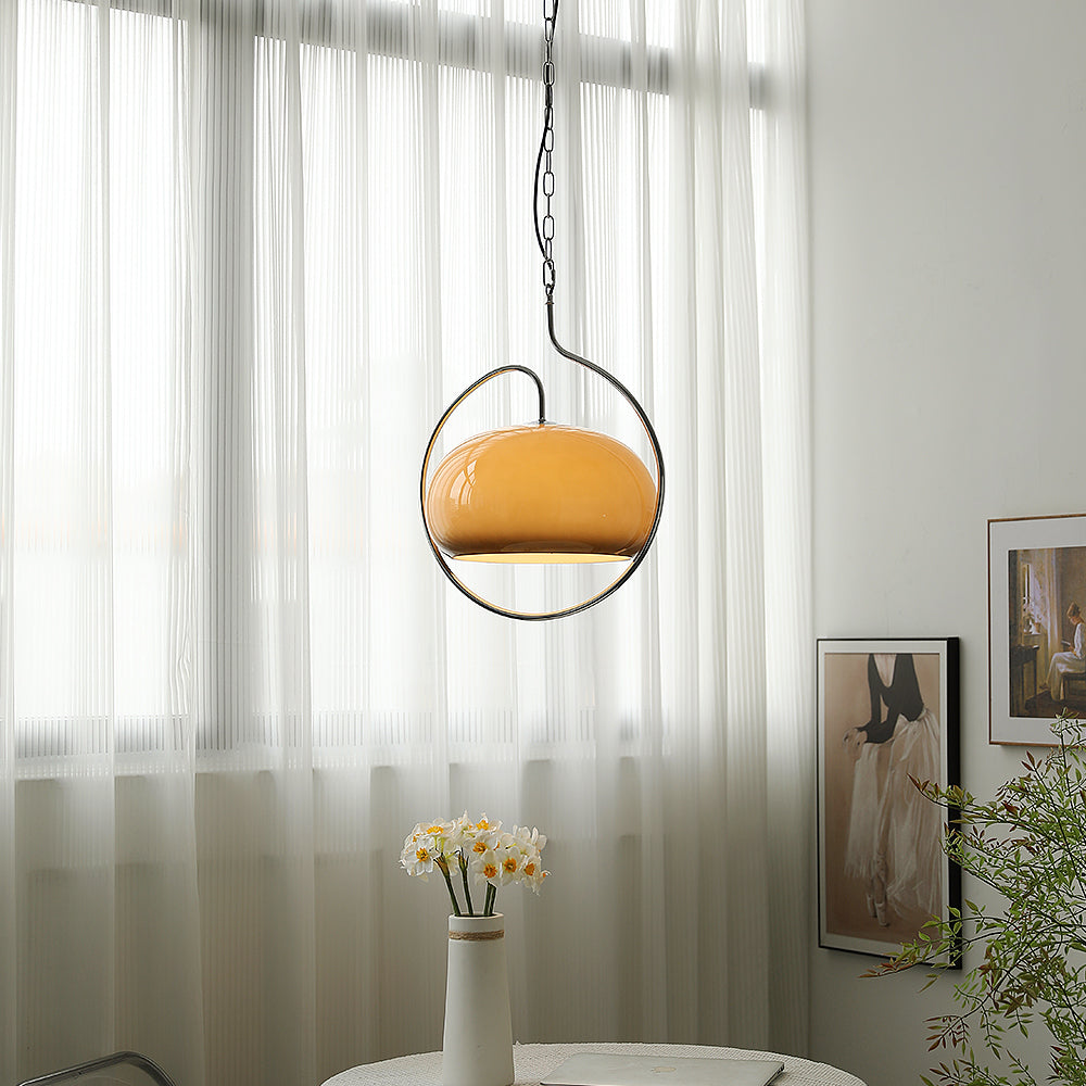 Brown glass Clérachic pendant in a chrome loop in front of white sheer curtains, with a vase of daffodils on a table below.