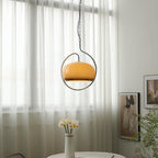 Brown glass Clérachic pendant in a chrome loop in front of white sheer curtains, with a vase of daffodils on a table below.