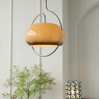 Brown glass Clérachic pendant with its chrome ring, seen in an arched white room with a green plant and a bead lamp below.