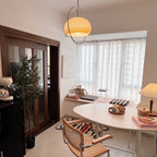 Clérachic pendant glowing amber above a dining room, with an oval white table, rattan chairs and a pleated table lamp.