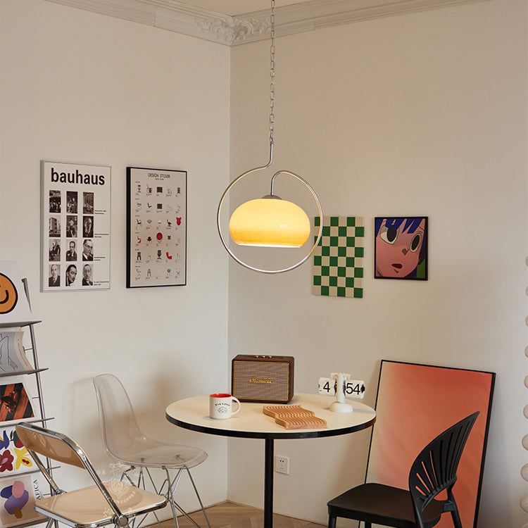 Lit Clérachic pendant with a yellow-cream glass dome, in a corner with Bauhaus prints, a round table and a retro speaker.