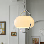 Large white glass dome of this Clérachic pendant inside its chrome ring, with framed pictures on a pale wall behind it.