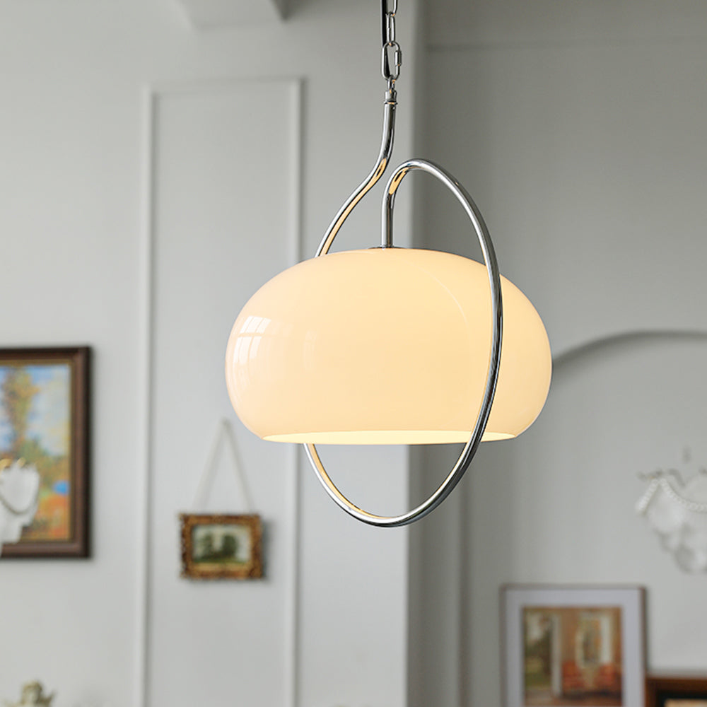 Large white glass dome of this Clérachic pendant inside its chrome ring, with framed pictures on a pale wall behind it.