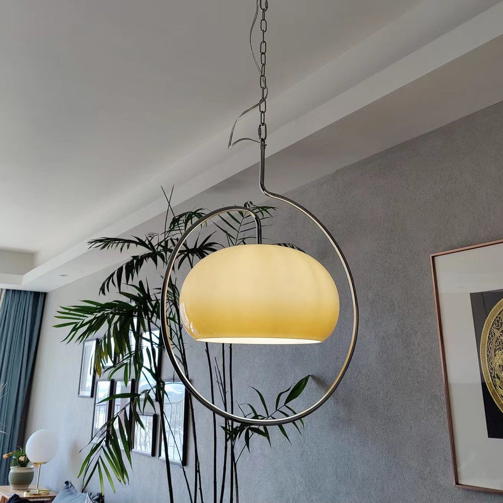 Clérachic pendant with a pale yellow glass dome, seen from below with a tall bamboo plant and a grey wall behind it.