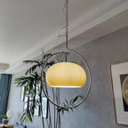 Clérachic pendant with a pale yellow glass dome, seen from below with a tall bamboo plant and a grey wall behind it.