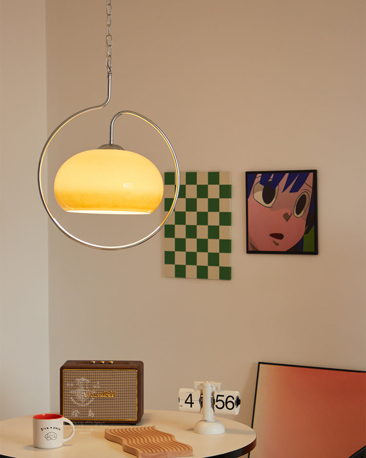 Clérachic pendant lit yellow-cream in a chrome ring, above a round table with a retro speaker, beside a green chequered print.