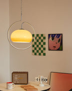 Clérachic pendant lit yellow-cream in a chrome ring, above a round table with a retro speaker, beside a green chequered print.