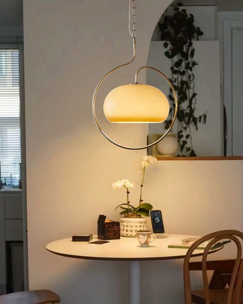 Clérachic pendant with a yellow-cream glass dome in a chrome ring, above a small round table with white orchids and a wooden chair.