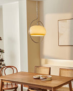 Clérachic pendant glowing warm cream above a timber dining table, with rattan chairs and a textured art print on the wall.