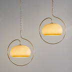 Pair of Clérachic pendants with yellow-cream glass domes in champagne-toned rings, hung at different heights against a grey backdrop.