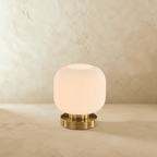 Clérachic ribbed glass dome table lamp in white with a brushed brass base, styled small and unlit on a plaster surface.