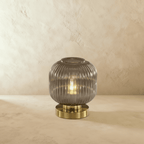 Clérachic ribbed glass dome table lamp in smoky gray with a brass base, tall silhouette lit warm on a plaster surface.