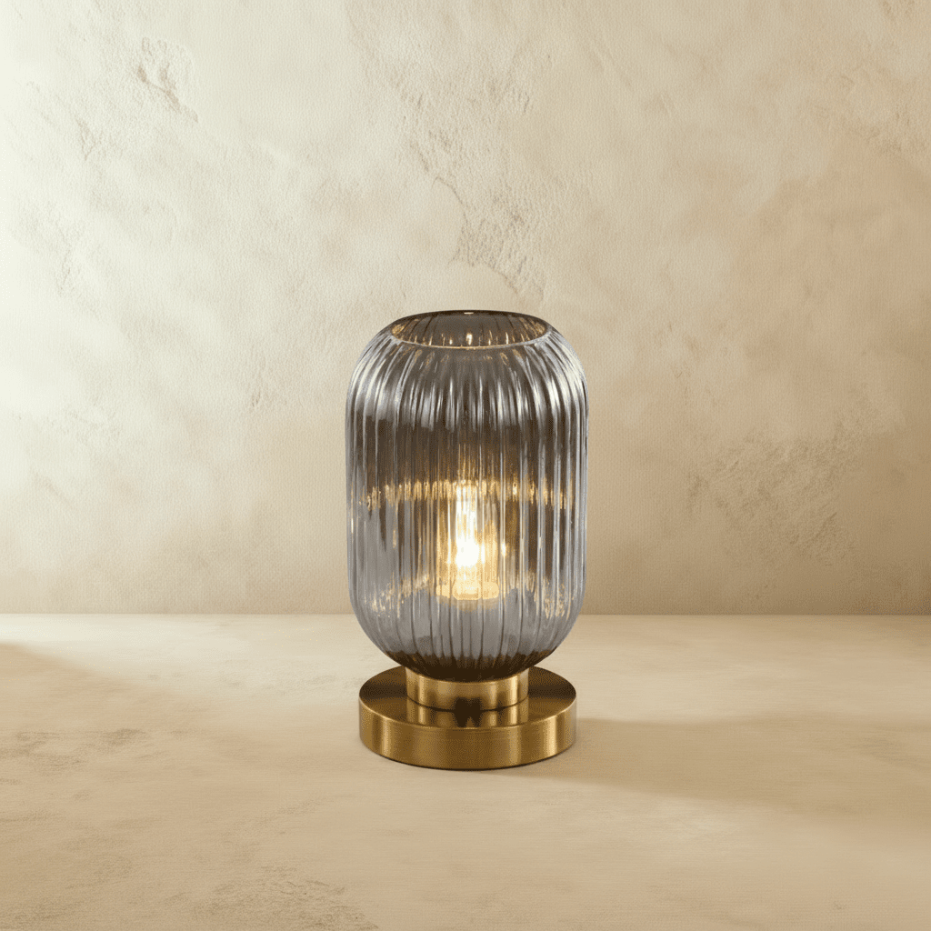 Clérachic ribbed glass dome table lamp in smoky gray, tall silhouette lit warm, brass base on a plaster surface.