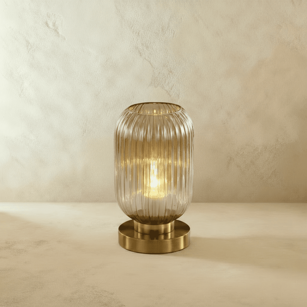 Clérachic ribbed glass dome table lamp in a clear tone, tall silhouette lit warm gold, brass base on a plaster surface.