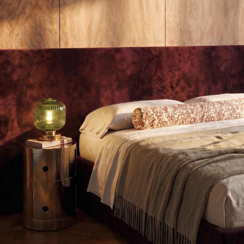 Clérachic ribbed glass dome table lamp in green, lit on a brass drum nightstand beside a burgundy velvet headboard.