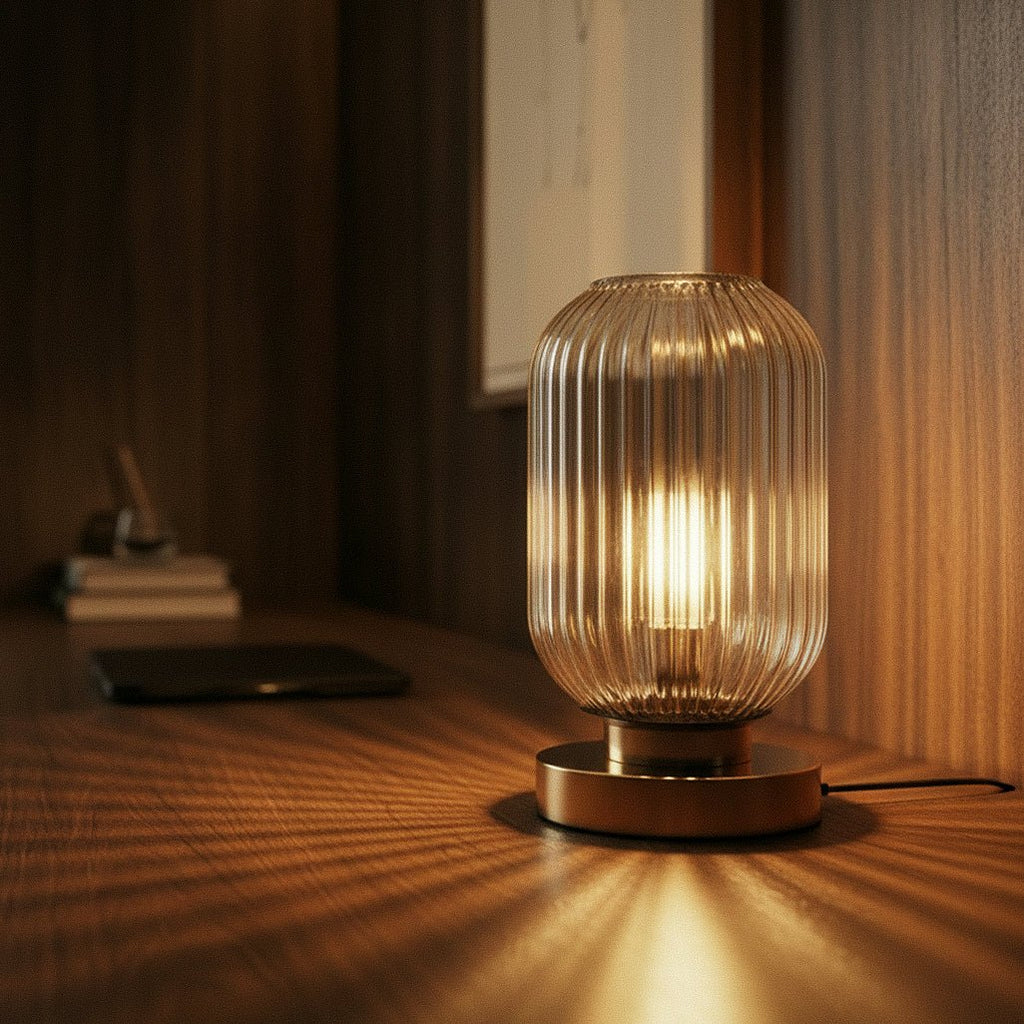 Clérachic ribbed glass dome table lamp in a clear tone, lit close on a walnut desk beside books and a phone.