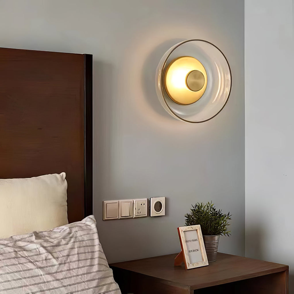 Above a bed with a walnut headboard and striped pillows, this Clérachic wall light glows warm through its clear glass dome.