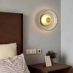 Above a bed with a walnut headboard and striped pillows, this Clérachic wall light glows warm through its clear glass dome.