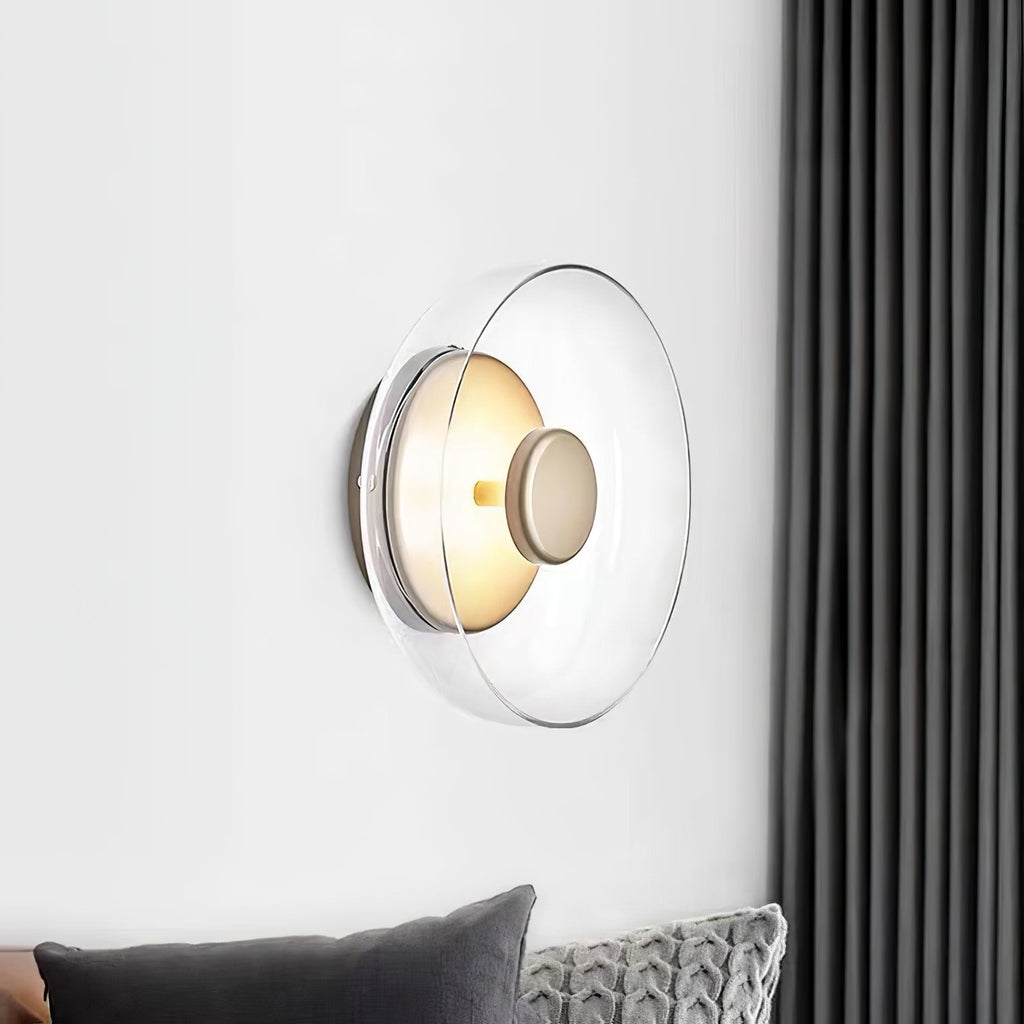 Mounted on a white wall beside a dark grey curtain, this Clérachic wall light has a clear glass dome and a brass centre knob.