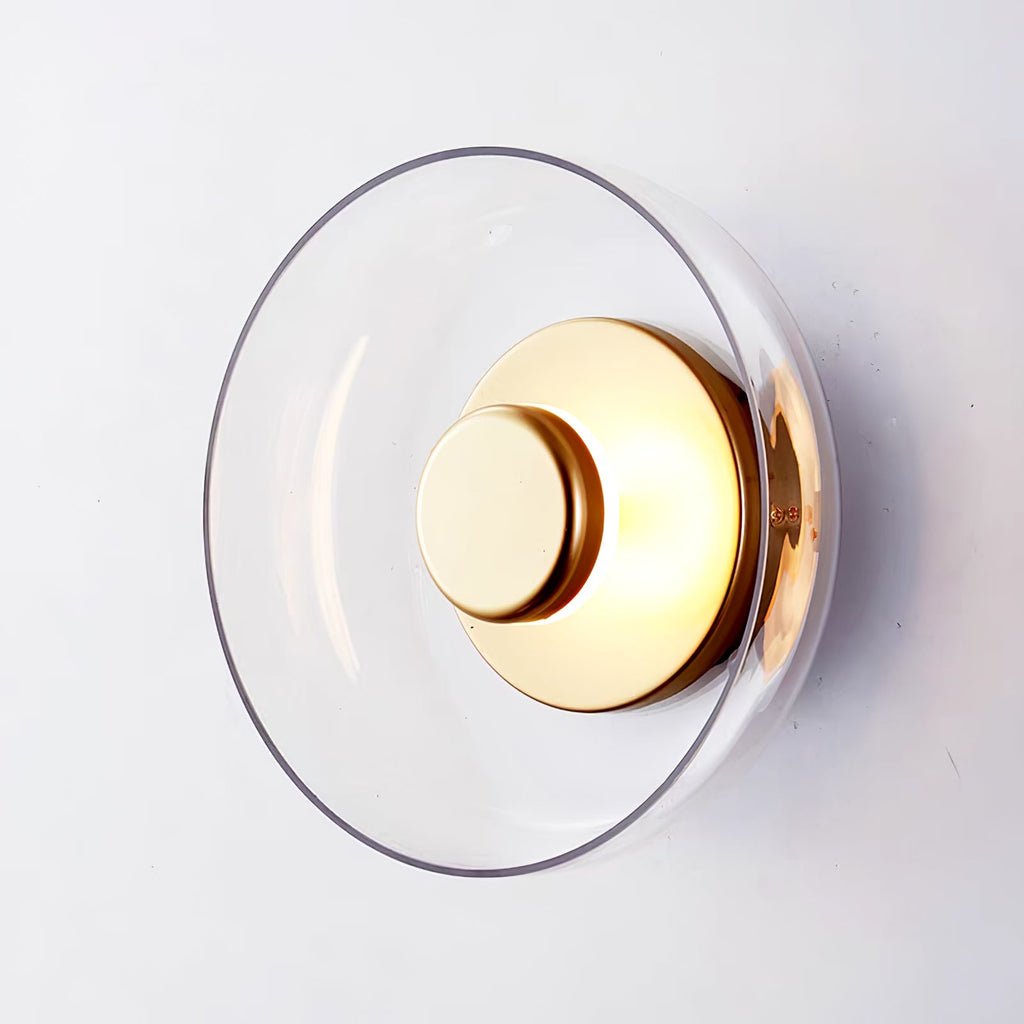 Close view of the clear glass dome and brushed brass centre disc of this Clérachic wall light on a pale wall.