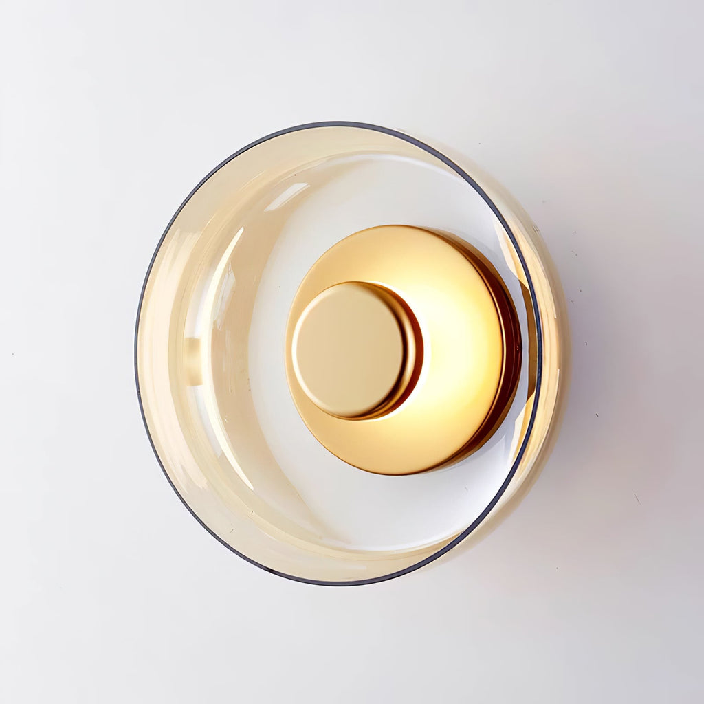 An amber glass version of this Clérachic wall light, shown unlit with a brass centre disc against a pale grey wall.