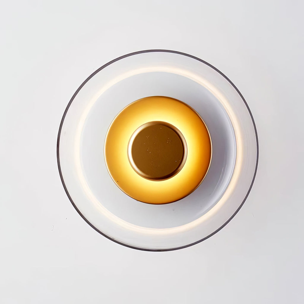 Front view of this Clérachic wall light lit, with a clear glass dome, a ring of light and a brass disc glowing at the centre.