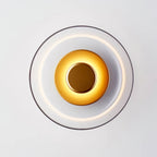Front view of this Clérachic wall light lit, with a clear glass dome, a ring of light and a brass disc glowing at the centre.