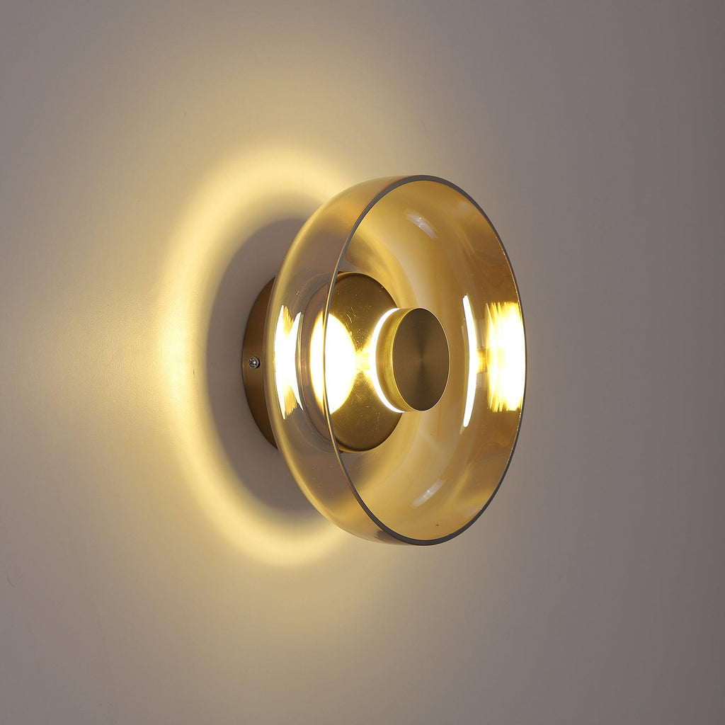 Warm light spreads across a taupe wall from this Clérachic wall light, whose pale amber glass dome sits on a brass back plate.