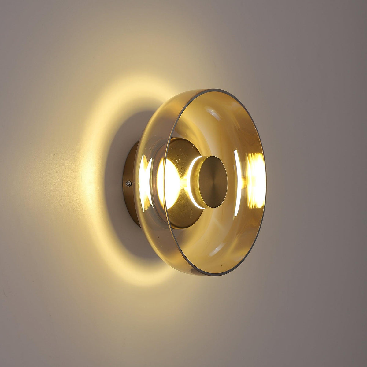 Warm light spreads across a taupe wall from this Clérachic wall light, whose pale amber glass dome sits on a brass back plate.