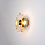 A Clérachic wall light with a smoky amber glass dome and a brass centre knob, glowing on a light wall.